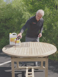Man showing results from using DiTEC teak furniture restoration kit's Triton 2.0 teak sealant on an outdoor teak table.